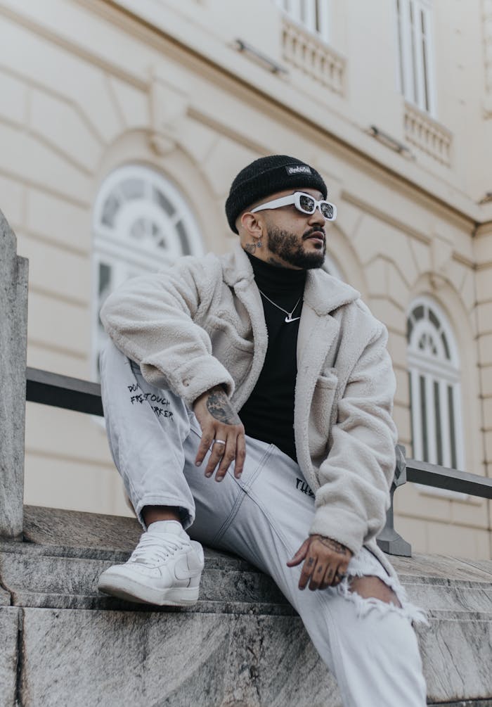 Stylish man in casual wear sits on urban steps, showcasing contemporary fashion.