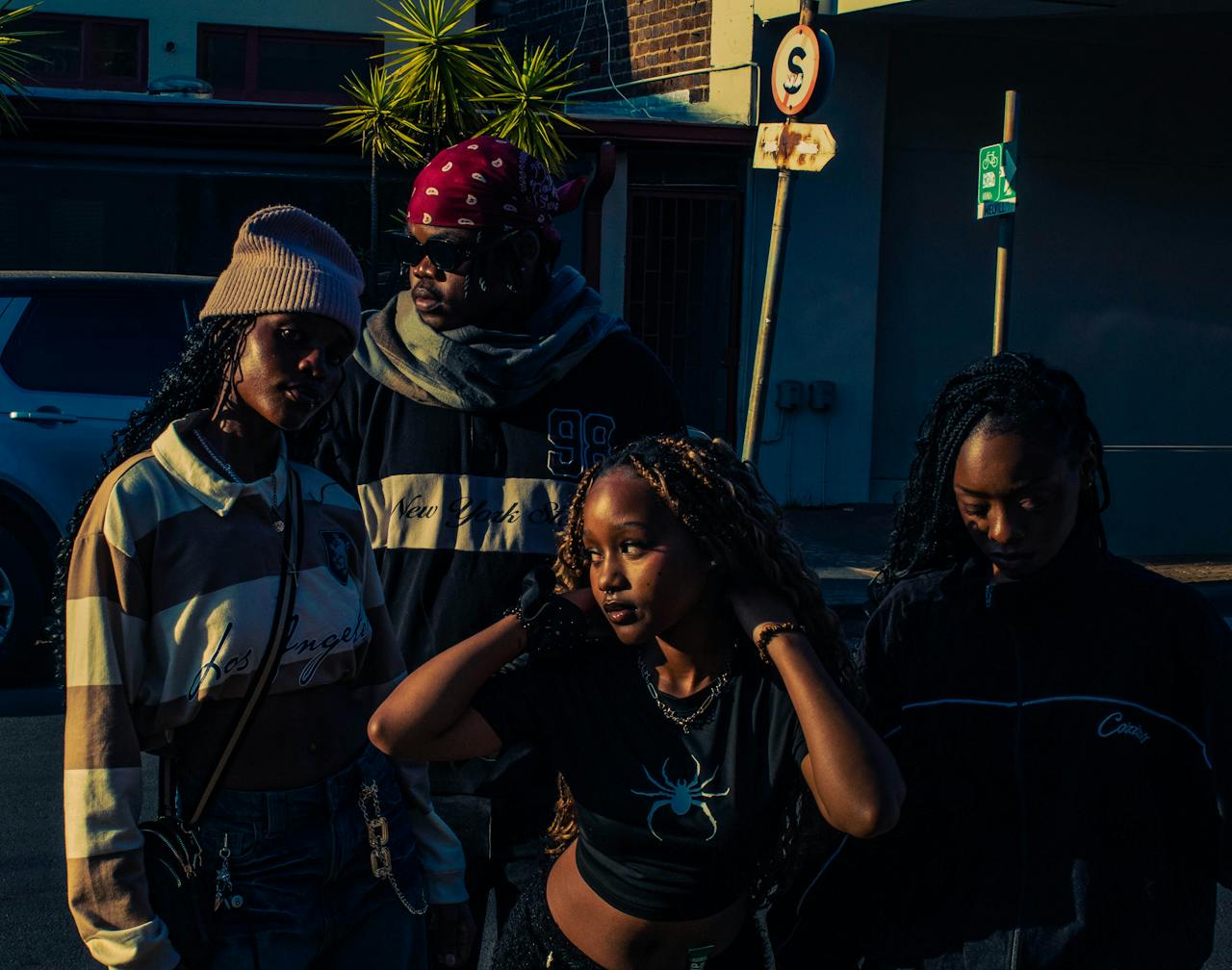 Group of young adults in stylish streetwear posing in urban nighttime setting.